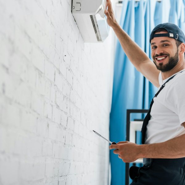 smiling-workman-looking-at-camera-while-repairing-air-conditioner.jpg